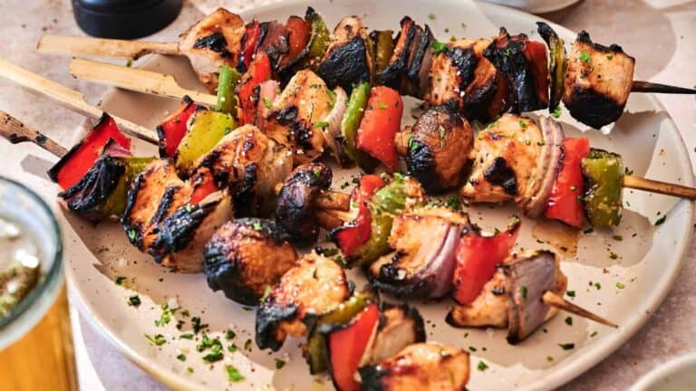 Grilled chicken skewers with red bell peppers, green bell peppers, and onions are served on a white plate, garnished with chopped herbs.
