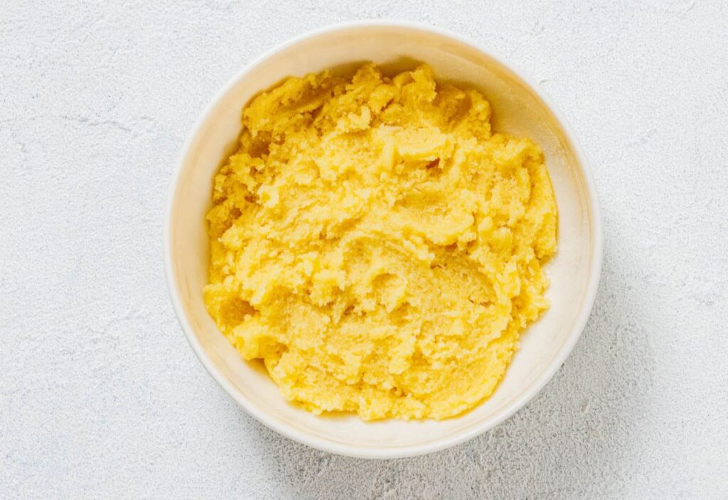 A bowl filled with freshly prepared yellow polenta on a light textured surface.