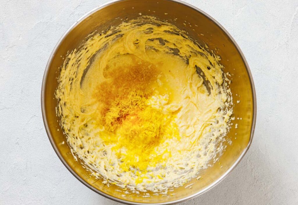 A mixing bowl with creamed butter and sugar, egg yolks, and lemon zest.