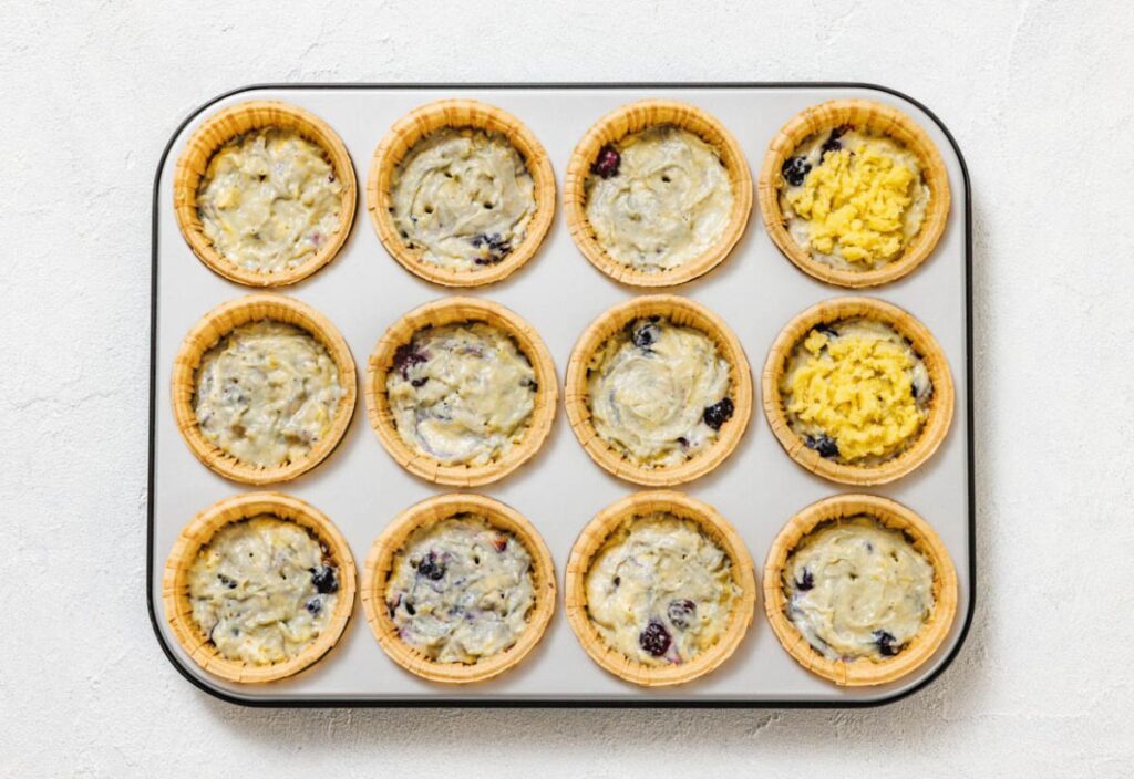 A muffin tin with twelve unbaked mini pies, some topped with crumble.
