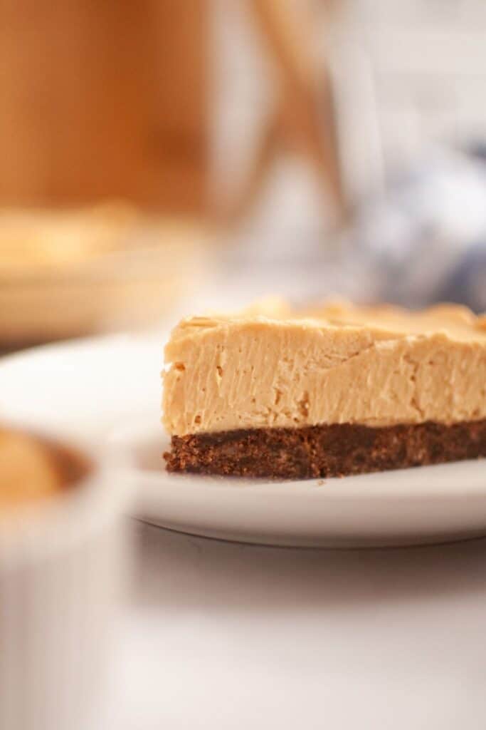 A slice of creamy peanut butter cheesecake with a chocolate crust on a white plate. Soft lighting creates a cozy, inviting atmosphere.