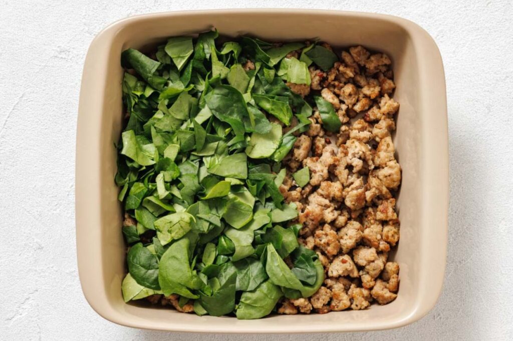 A baking dish layered with cooked sausage meat and spinach.