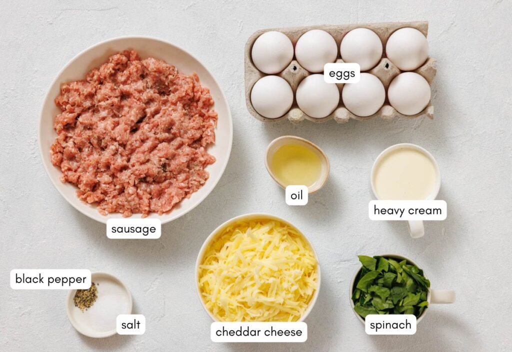 Top view of all the ingredients needed to create Sausage and Egg Breakfast Casserole, including sausage, eggs, heavy cream, oil, cheddar cheese, spinach, salt, and pepper.