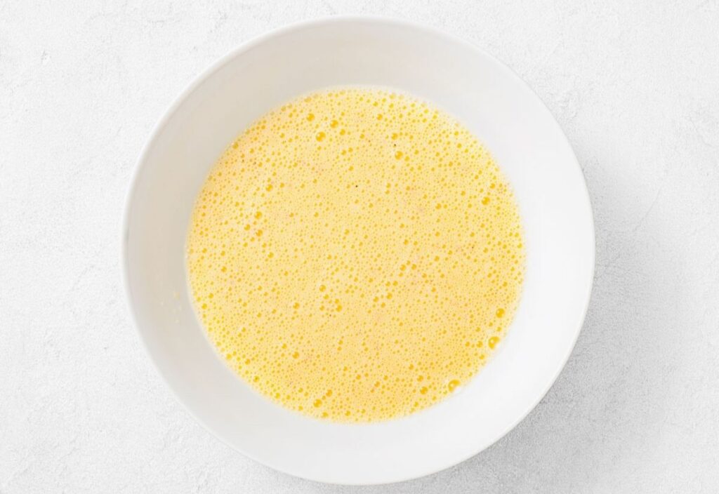 White bowl with frothy beaten eggs.