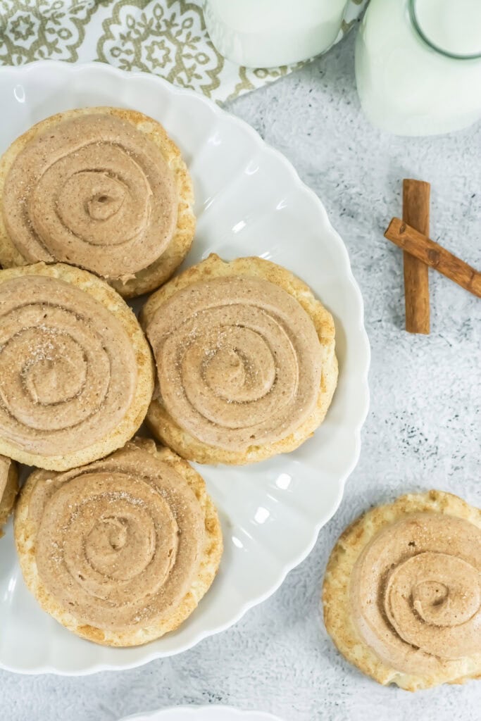 Cinnamon cookies with swirl icing on a white plate, surrounded by milk bottles and cinnamon sticks, evoke a cozy and inviting atmosphere.