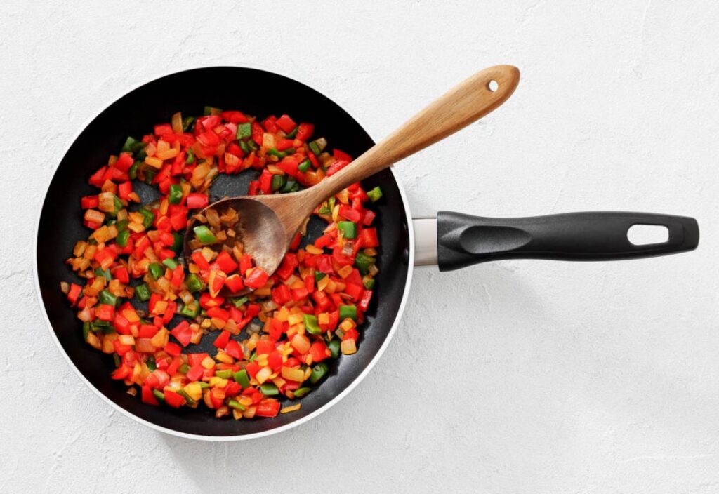 Black frying pan with sautéed red, green, and orange bell peppers.