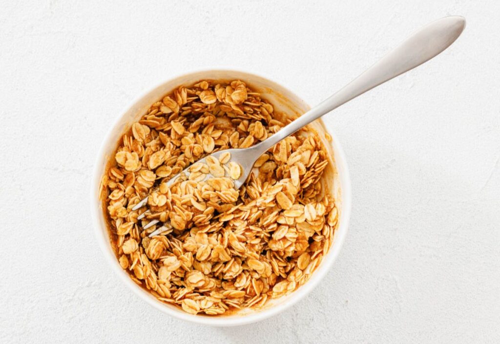 White bowl filled with glossy oats coated in a brown mixture, with a metal fork resting inside, placed on a clean white background.
