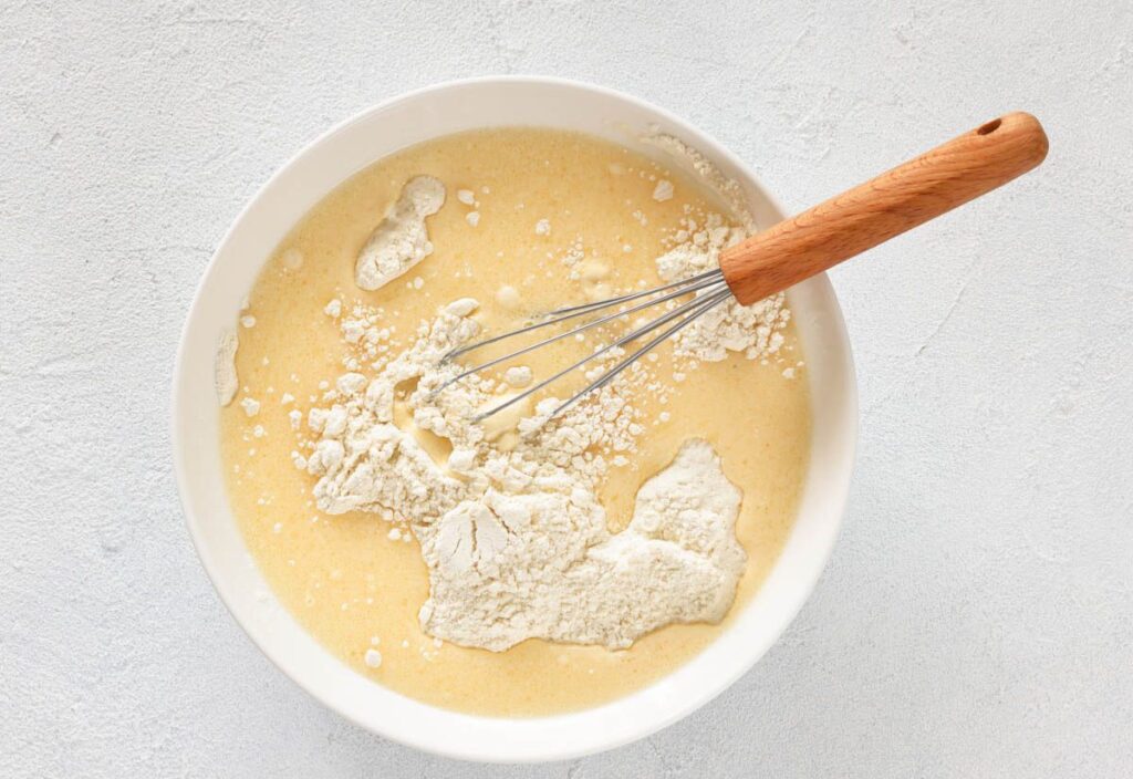 The mixture of liquid with flour being added to it, with flour scattered over the surface.