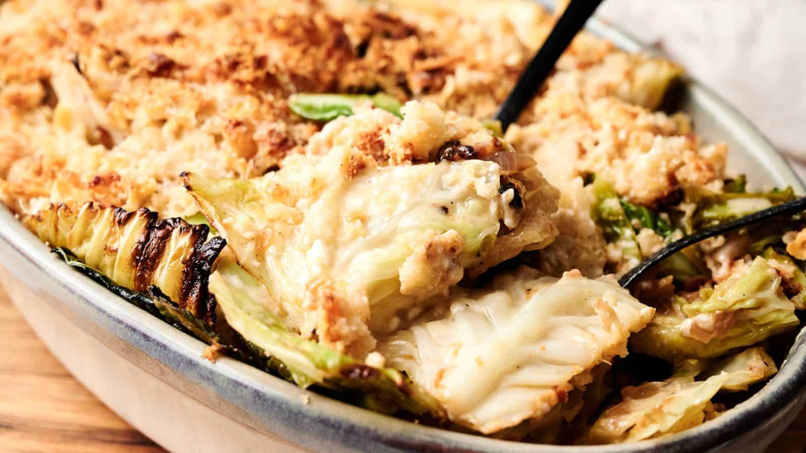 A close-up of a baked casserole dish filled with creamy cabbage gratin, topped with a golden breadcrumb crust, with a serving spoon partially visible.