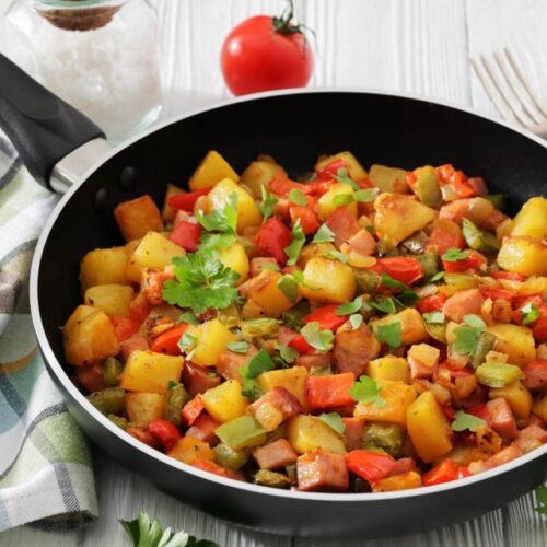 A skillet filled with colorful sautéed vegetables, including potatoes, red and green peppers, garnished with parsley. A vibrant, fresh meal setting.