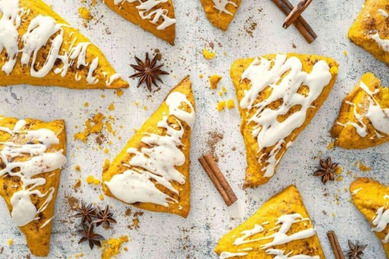 Pumpkin Spice Scones with Vanilla Glaze are arranged on a light surface, surrounded by cinnamon sticks and star anise.