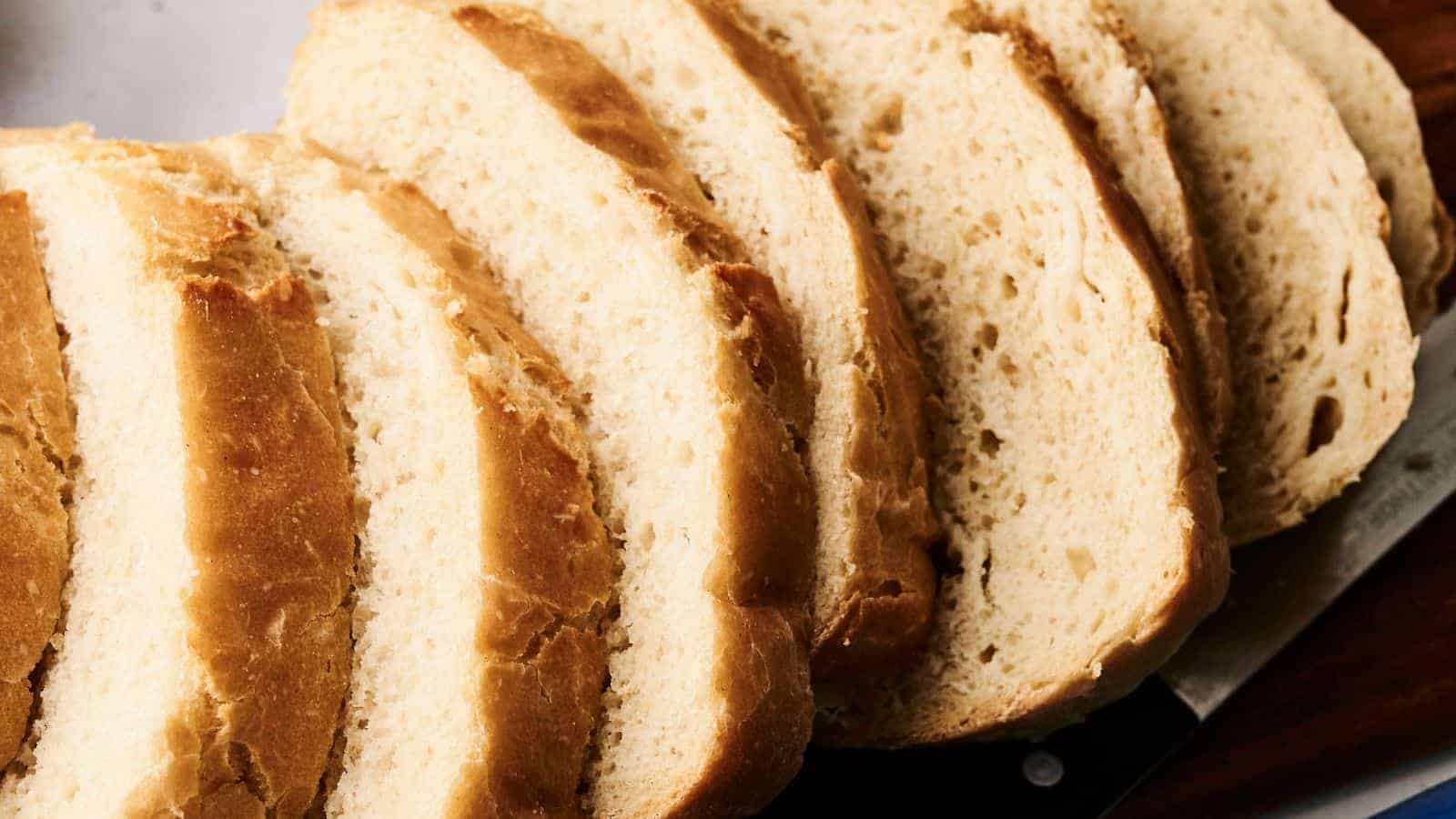 Sliced loaf of bread on a cutting board with a knife beside it.