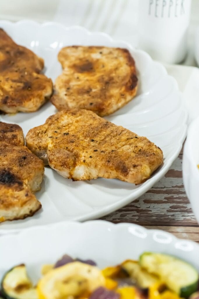 Broiled Pork Chops with a golden crust on a white plate, seasoned with spices. The scene is inviting and warm, suggesting a homemade meal.