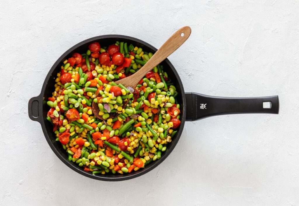 A skillet full of succotash with a wooden spoon.