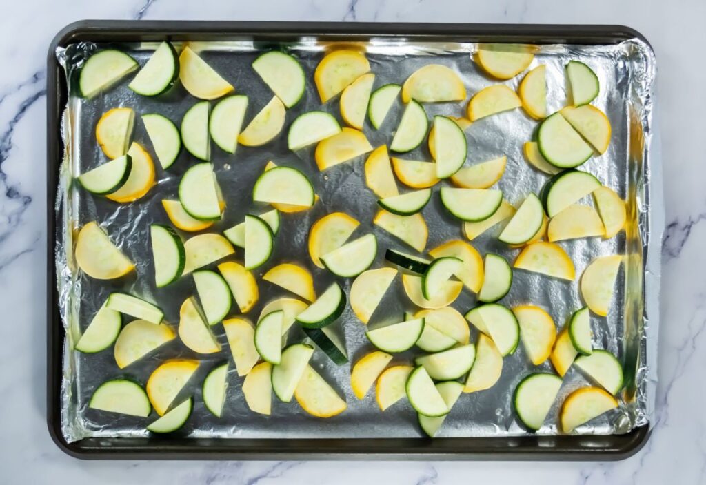 Layered zucchinis and squash on the lined baking sheet.