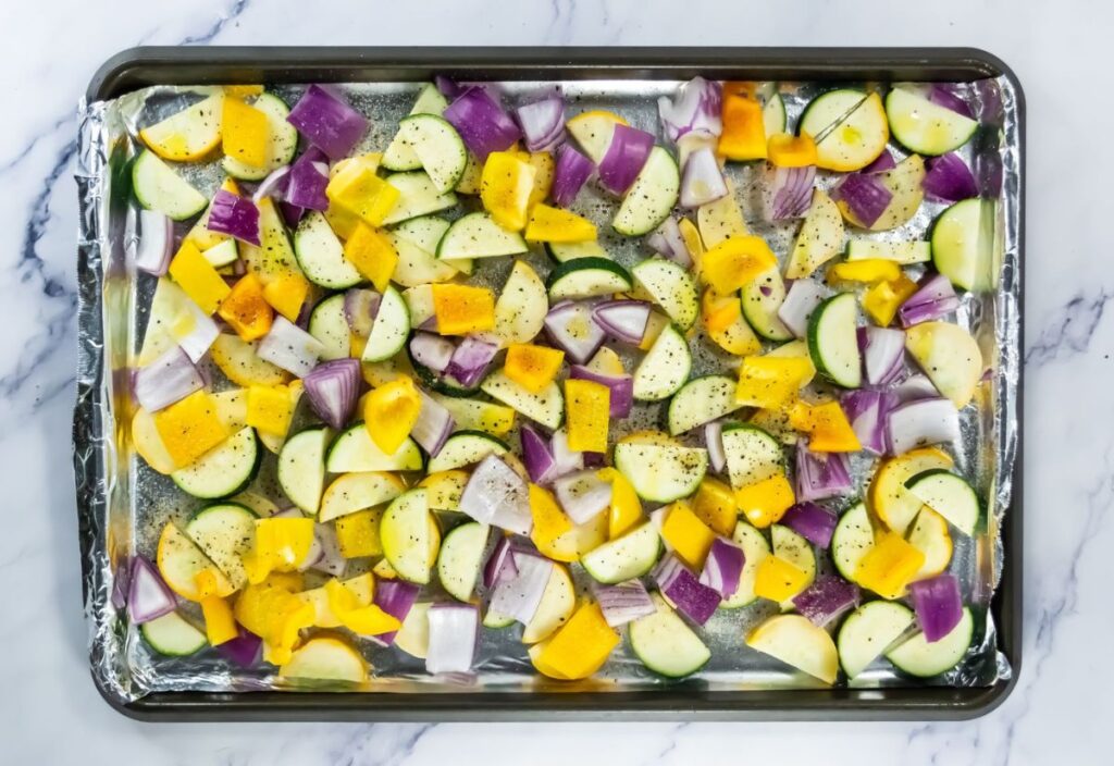 A seasoned chopped vegetables in a lined baking sheet.