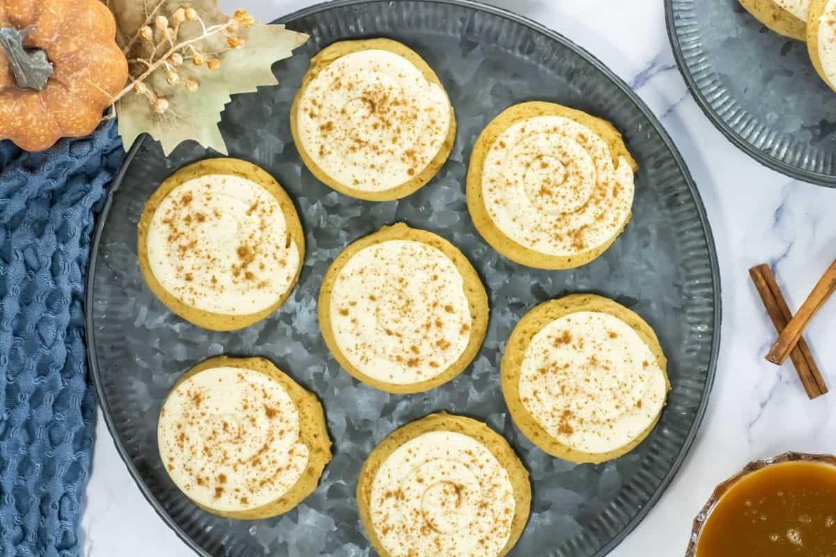 Crumbl Caramel-Pumpkin Cookies are arranged on a metal tray, accompanied by fall-themed decorations and cinnamon sticks.