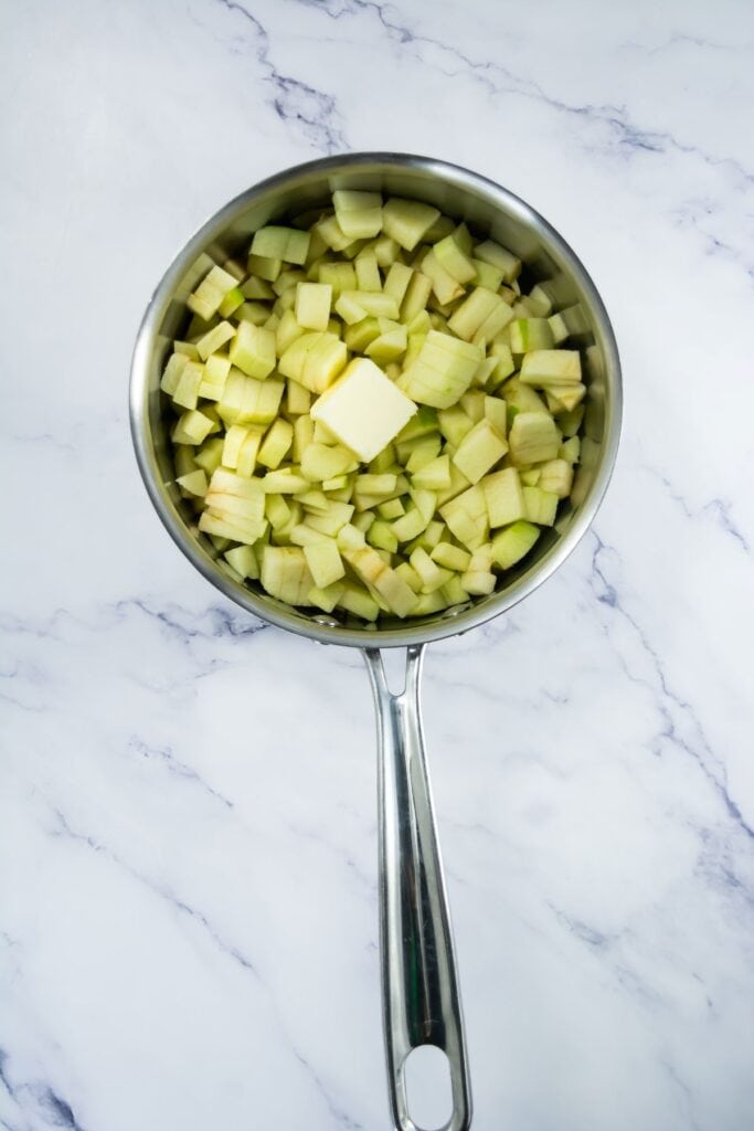 A close-up of chopped green apples with a cube of butter placed in the center of the pan.