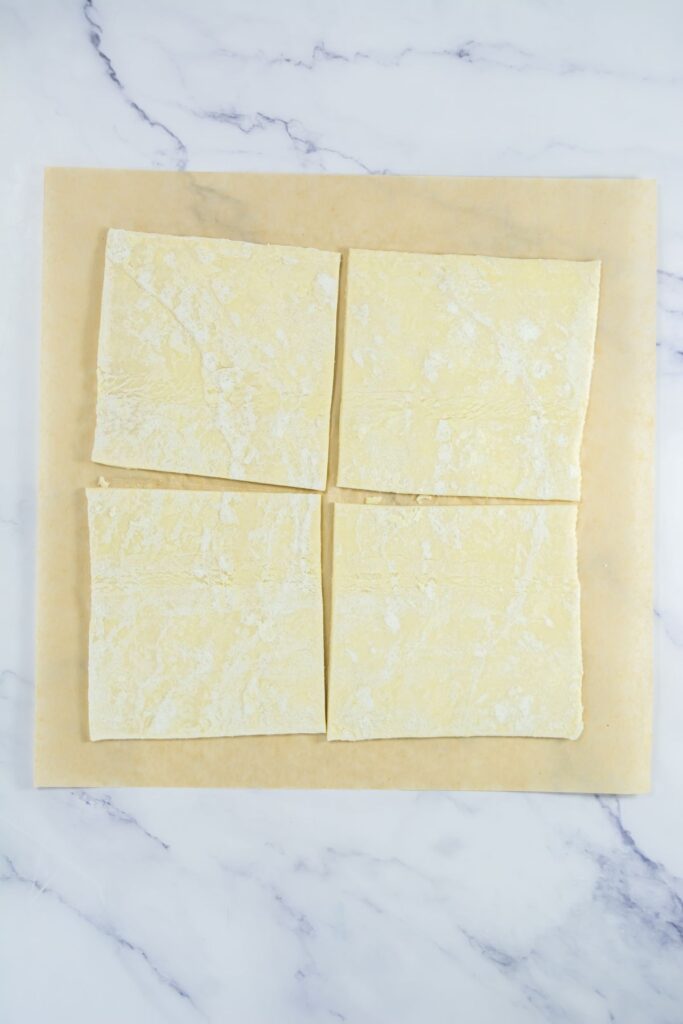 Puff pastry sheets laid flat on parchment paper, cut into four squares.