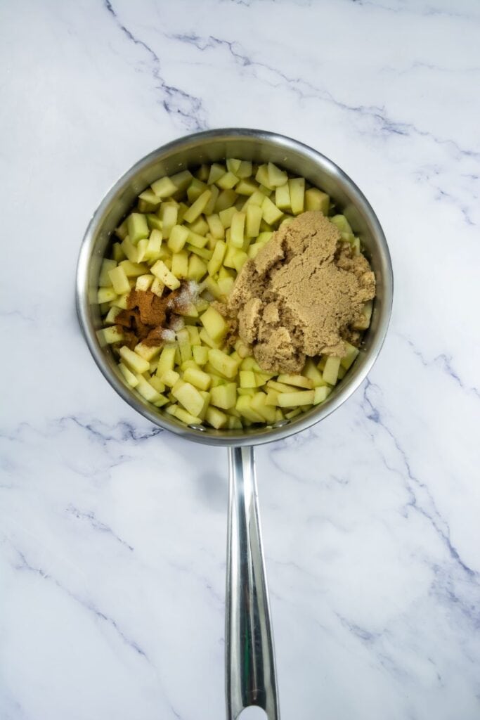 A stainless steel pan with chopped green apples, brown sugar, cinnamon, and a pinch of salt, all ready to be cooked.