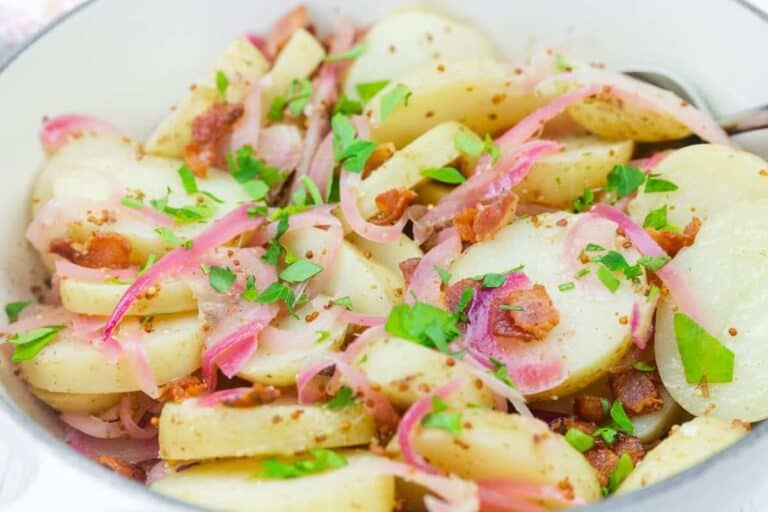 Chef Jenn’s Warm German Potato Salad with sliced potatoes with bacon, red onions, and chopped parsley, served in a white bowl.