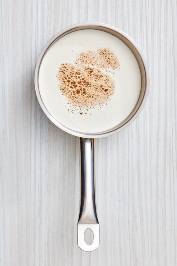 A close-up shot of milk in a saucepan with a dusting of ground cinnamon on top