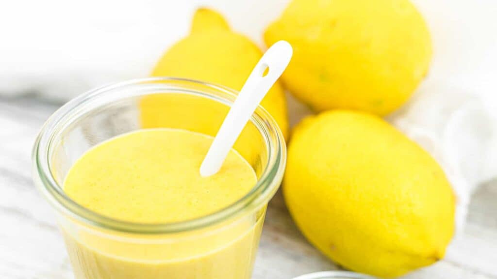 Keto Lemon Curd inside a glass with fresh lemons behind.