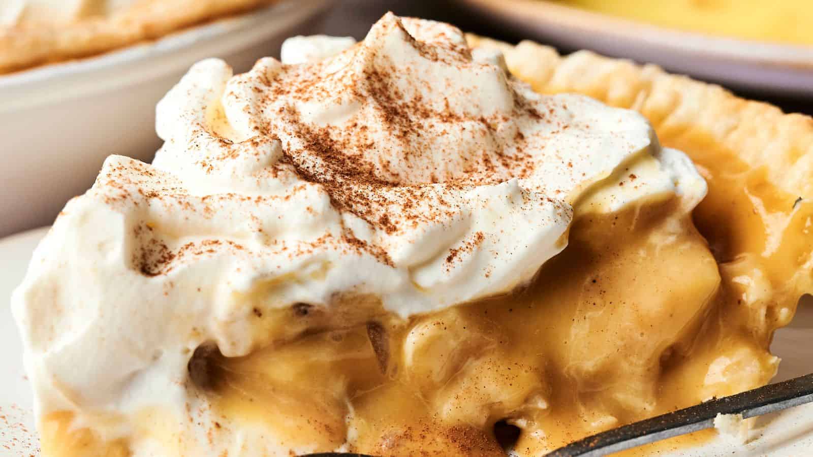 A slice of banana cream pie topped with whipped cream and a sprinkle of cinnamon on a plate.