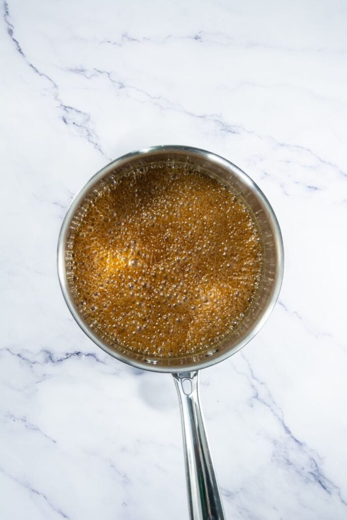 Close-up of bubbling caramel being prepared in a pan, showing the caramelized sugar mixture as it boils.
