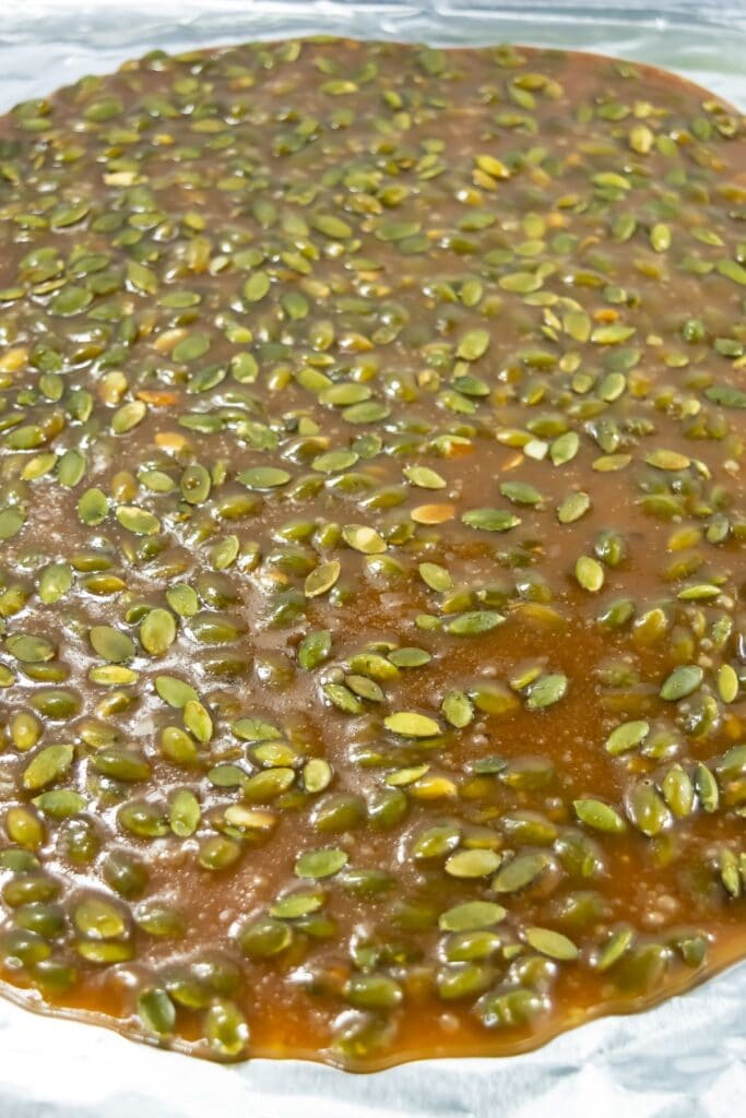 Pumpkin seed brittle cooling on a baking sheet, showing the mixture spread out and setting.