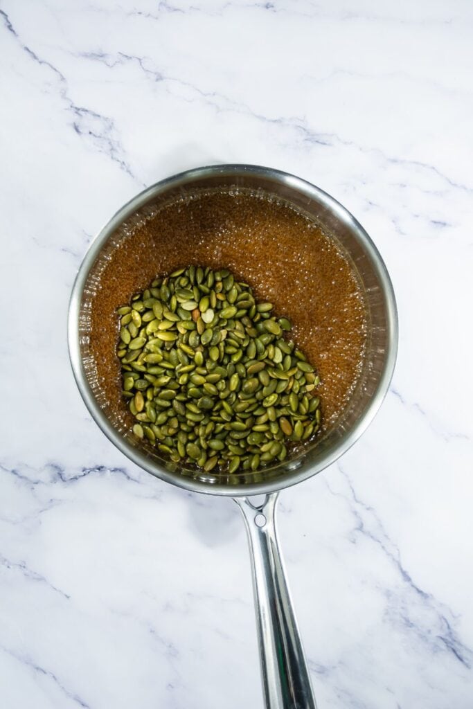 A saucepan with the caramel and pumpkin seeds mixed together before pouring onto the baking sheet to set.