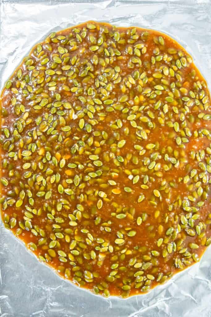 Pumpkin seed brittle cooling on a baking sheet, showing the mixture spread out and setting.