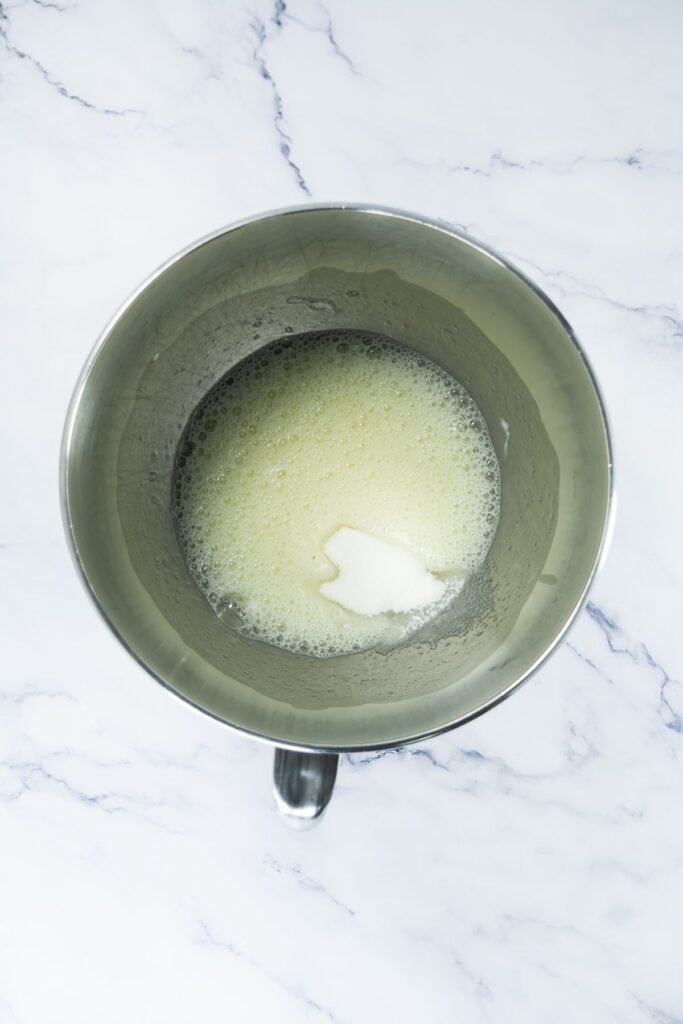 Mixed egg whites and cream of tartar in a mixing bowl, with added sugar.