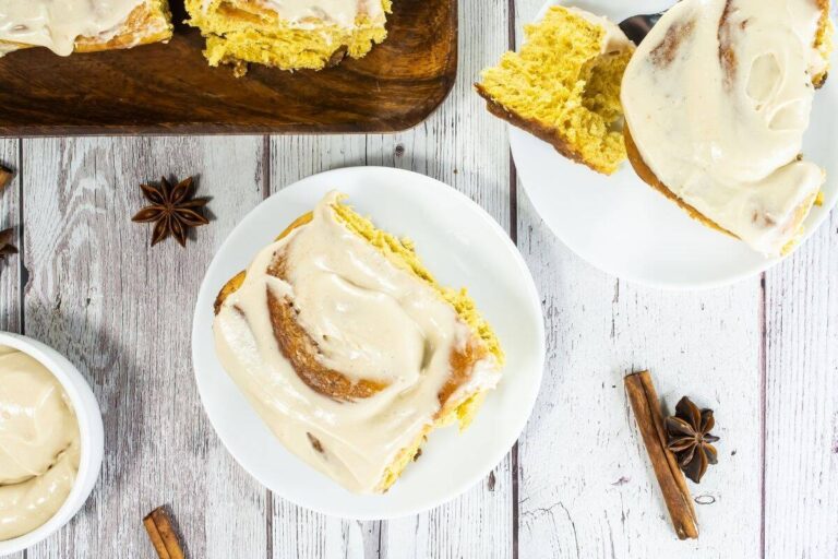 Homemade cinnamon rolls with cream cheese frosting on wooden serving board.