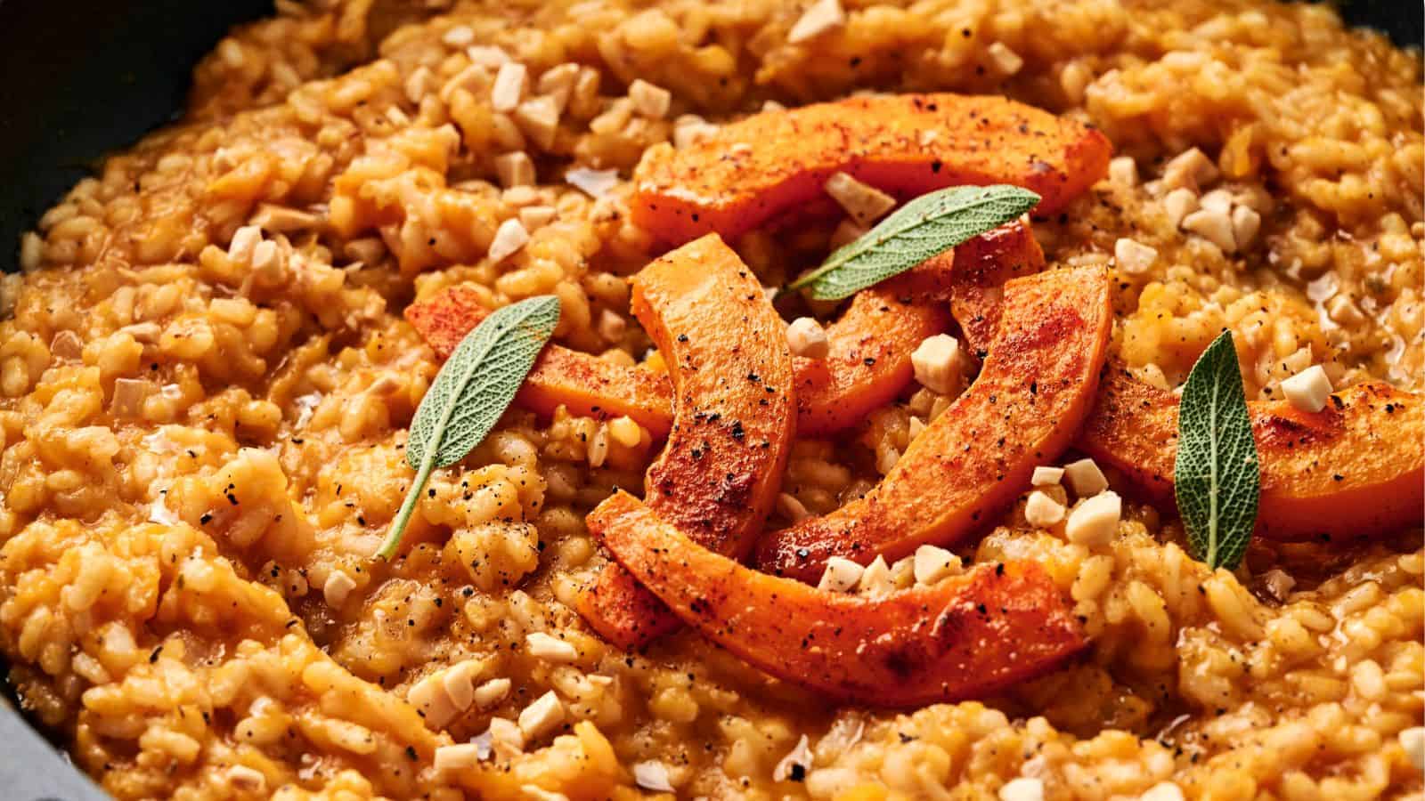 A close-up of vegan pumpkin risotto, topped with roasted pumpkin slices, sage leaves, and chopped nuts.