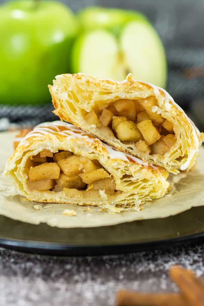 Close-up of an apple turnover with flaky pastry, filled with soft, cinnamon-spiced apple filling and drizzled with icing.