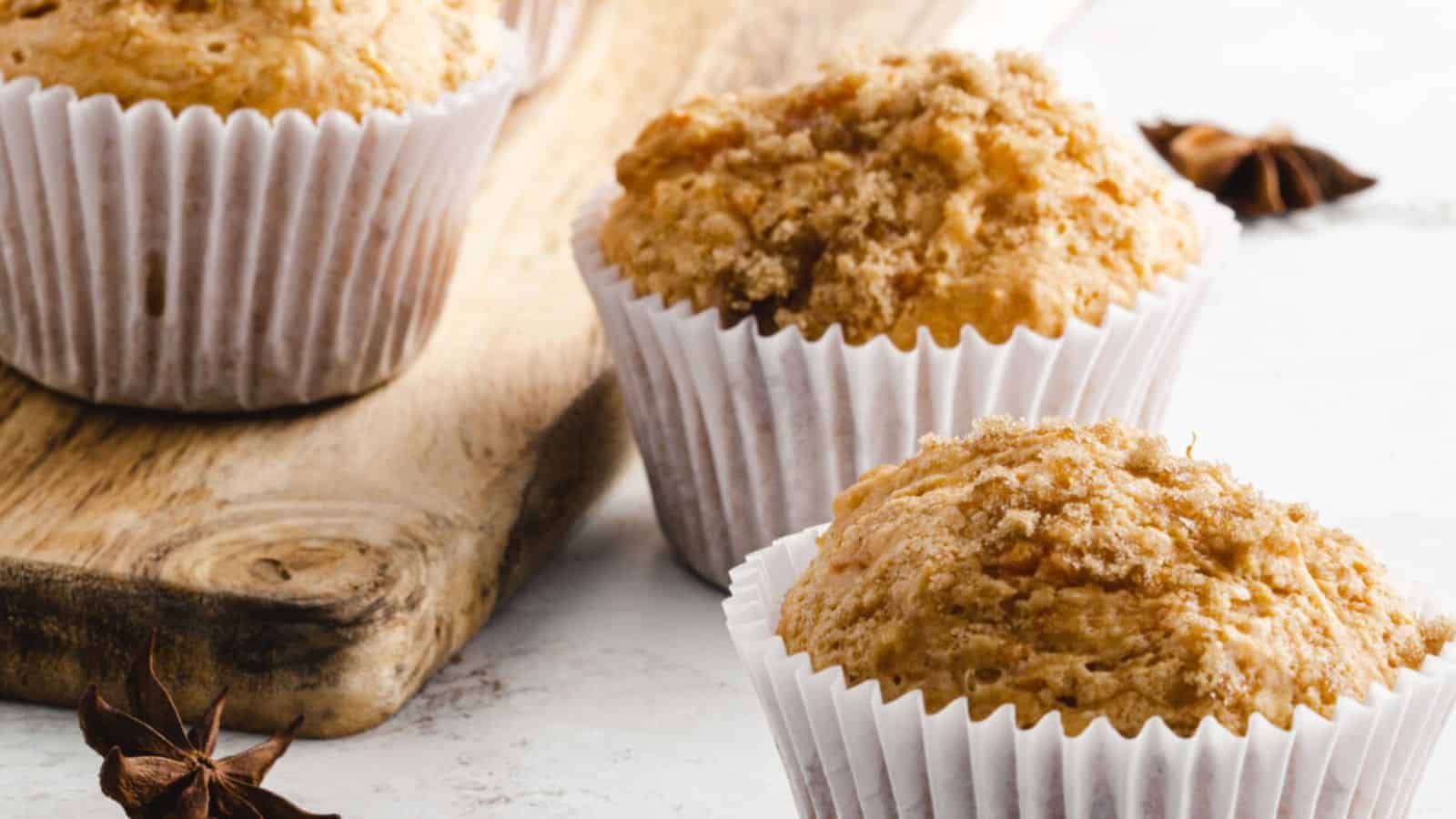Sweet potato muffins in white paper liners on a wooden board, topped with a crumbly brown sugar streusel.