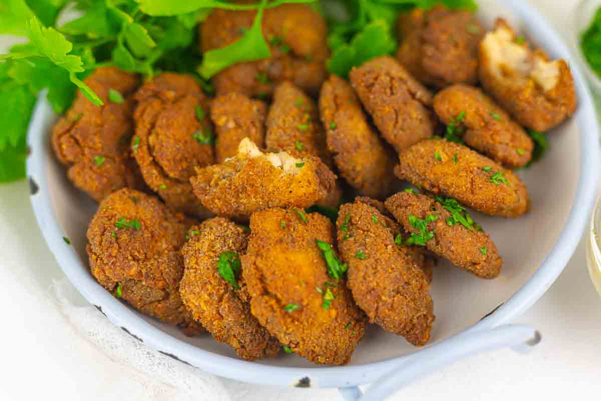 A plate filled with crispy, golden-brown fried chicken nugget pieces garnished with chopped parsley.