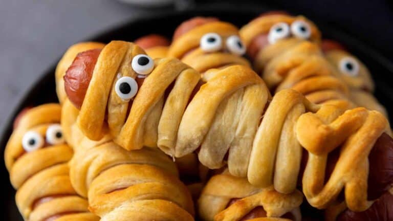 A close-up of baked hot dogs wrapped in dough resembling mummies, with googly eyes attached.
