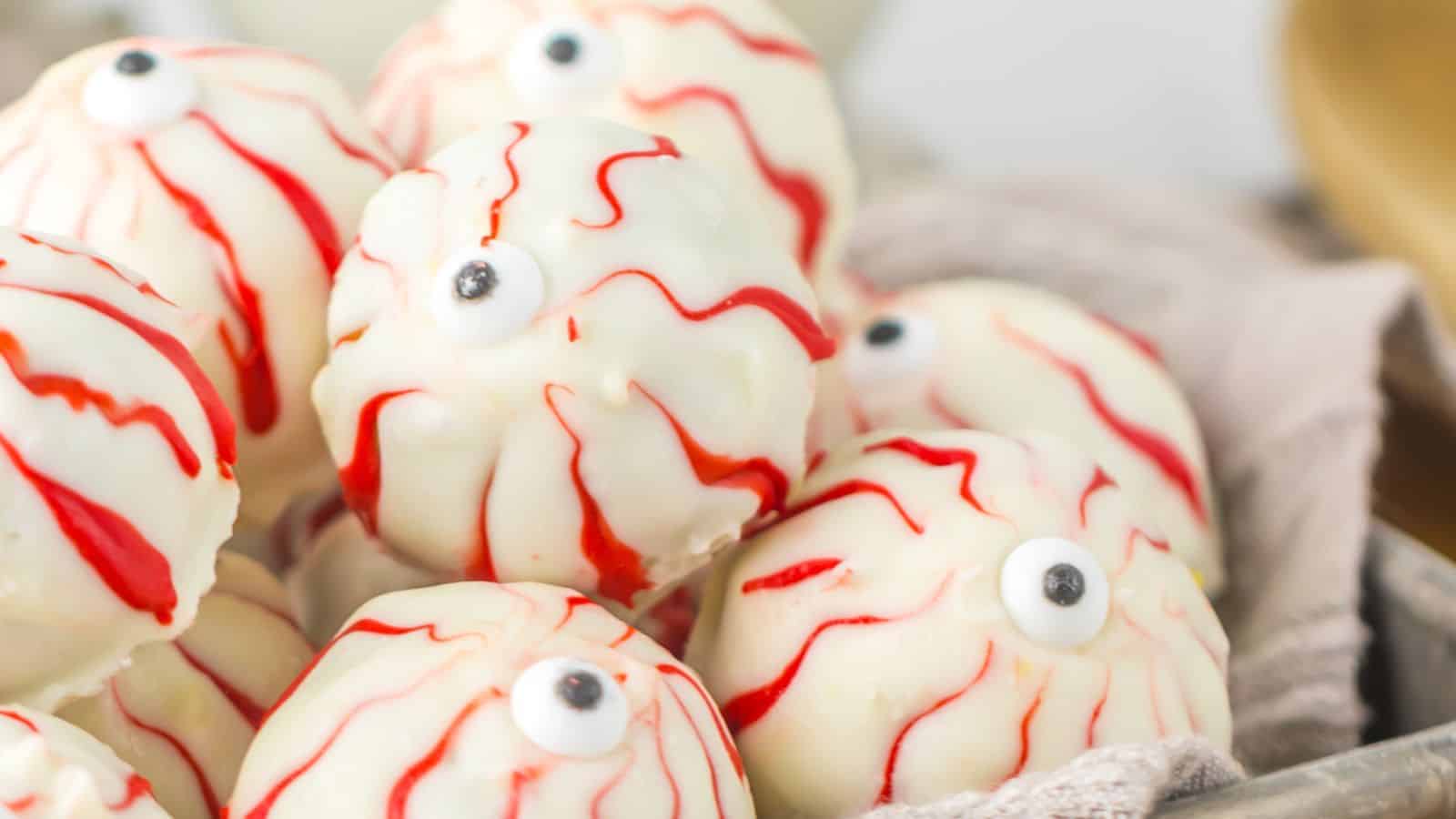 A pile of white chocolate covered truffles decorated to look like spooky Halloween eyeballs, complete with red veins and a candy eyeball in the center.