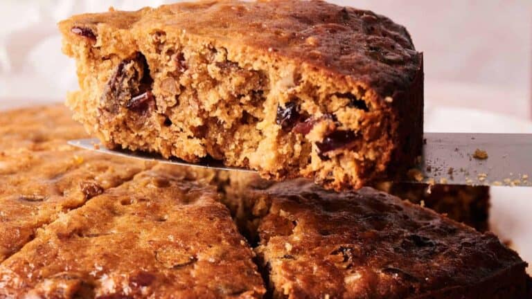 A moist fruit cake filled with mixed dried fruits, nuts, and spices, served on a plate with a decorative garnish.