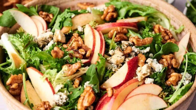 A salad with sliced honeycrisp apples, greens, and walnuts.
