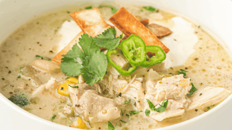A bowl of chicken tortilla soup topped with tortilla strips, cilantro, jalapeños, and a dollop of sour cream.