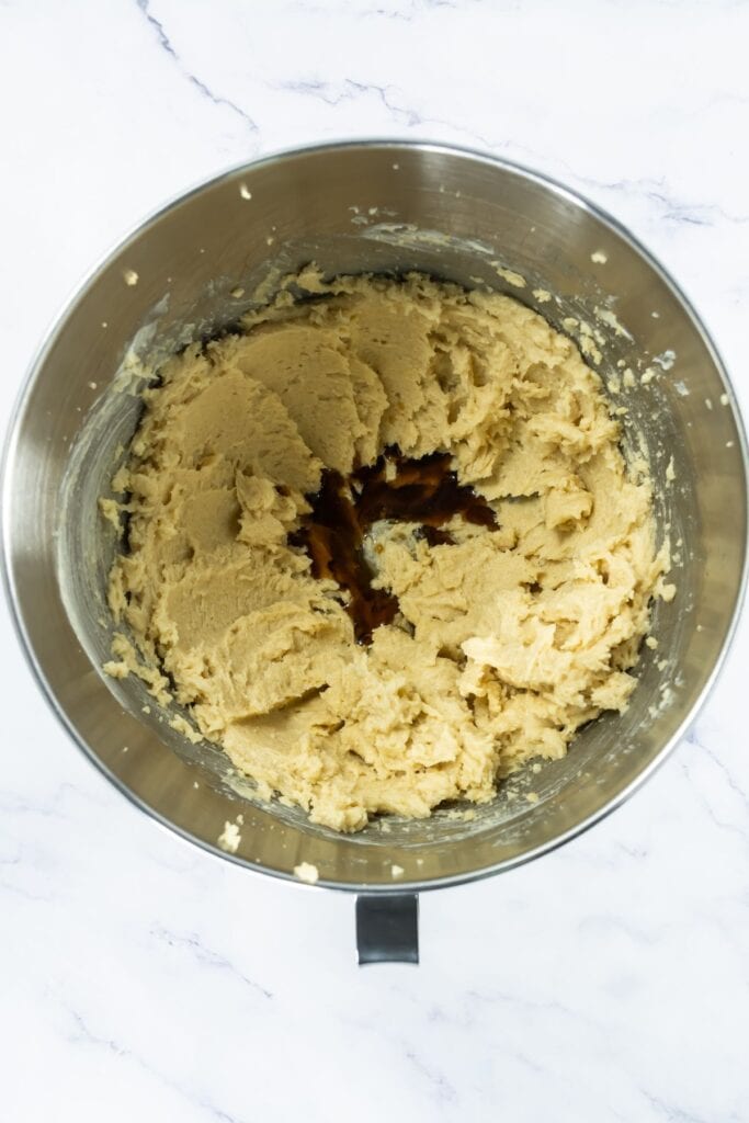 Stand mixer bowl filled with creamed butter and sugars with vanilla added to the center.