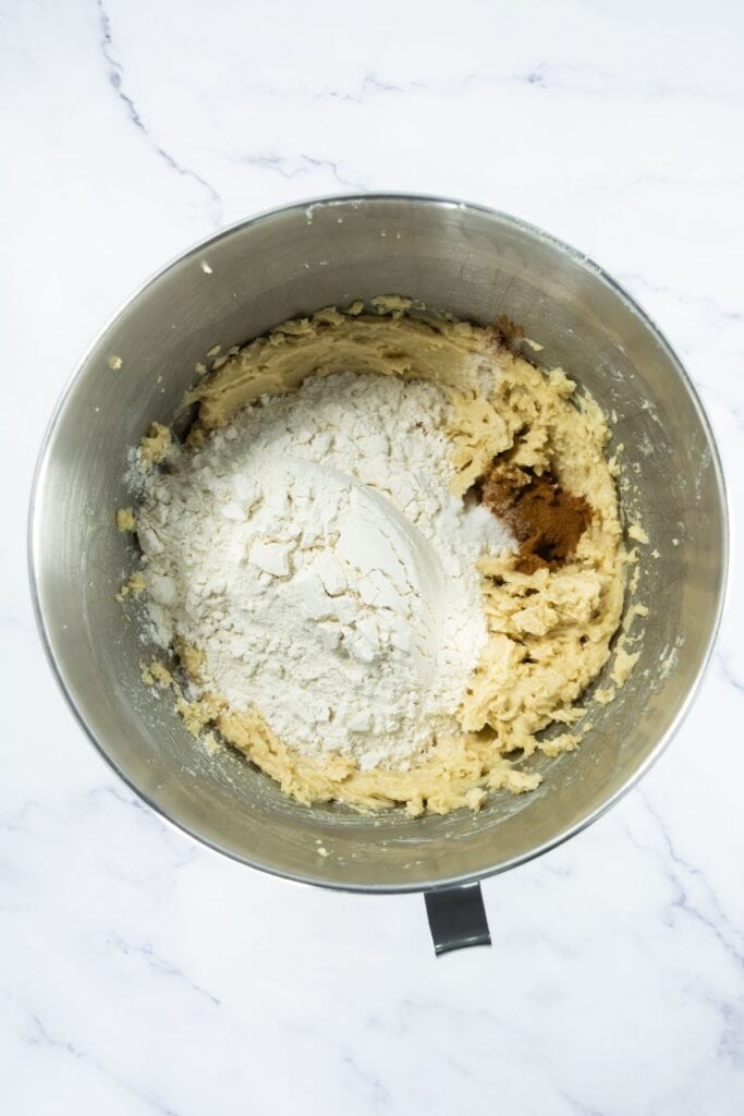 Flour, cinnamon and salt sitting on top of the creamed butter mixture in a mixing bowl.