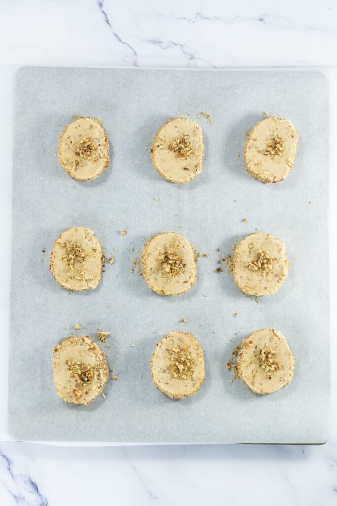 Nine slices of pecan shortbread dough arranged evenly on a parchment-lined baking sheet.