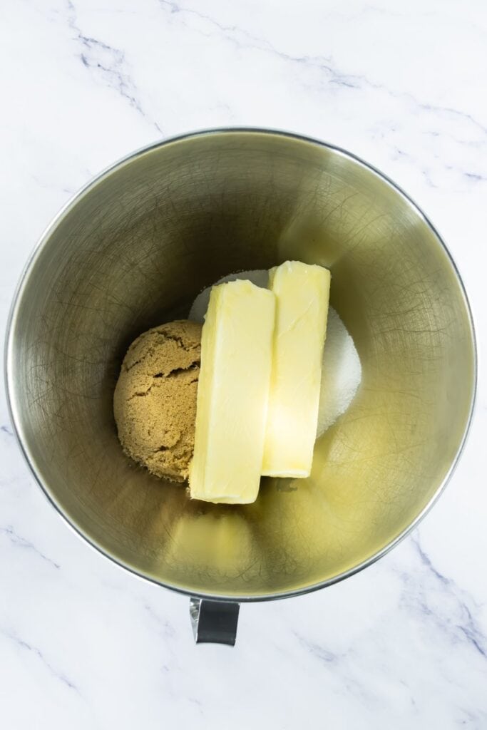 Sticks of butter, brown sugar and granulated sugar placed together in a metal mixing bowl.