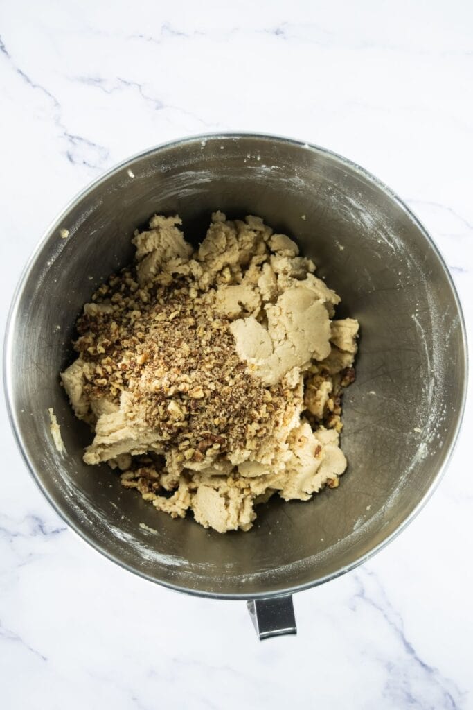 Chopped pecans added on top of the mixed shortbread dough in a metal bowl.