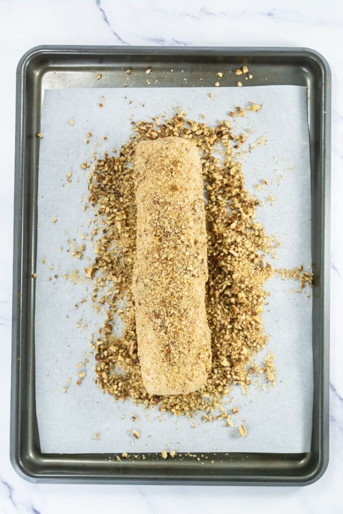 Pecan shortbread dough log fully coated in chopped pecans and turbinado sugar on a parchment-lined baking sheet.