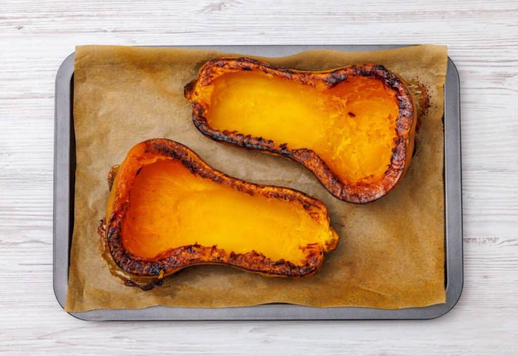 Roasted butternut squash halves with caramelized edges resting on a parchment-lined baking sheet.